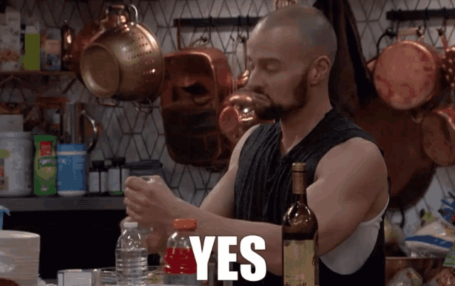 a man in a kitchen with a bottle of wine and the word yes behind him