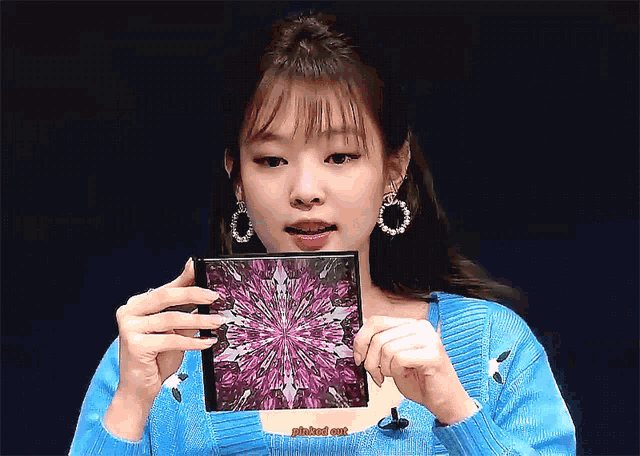a woman in a blue sweater is holding a cd with a purple design