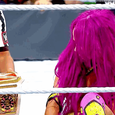 a woman with purple hair is sitting in a wrestling ring with a referee .