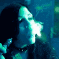 a woman is smoking a cigarette in a dark room with green lights behind her .