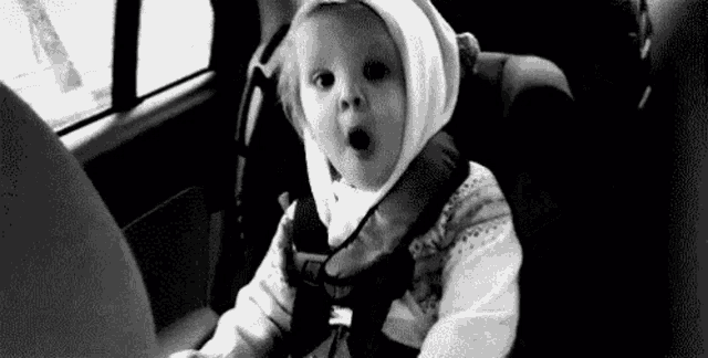 a baby is sitting in a car seat with his mouth open and wearing a hat .