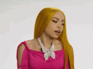 a woman with long yellow hair is wearing a pink top and a butterfly necklace