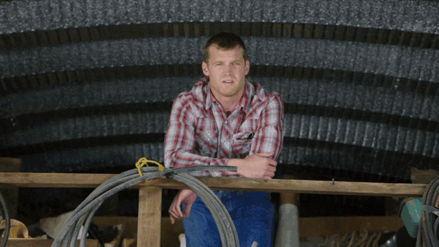 a man in a plaid shirt is sitting on a wooden beam
