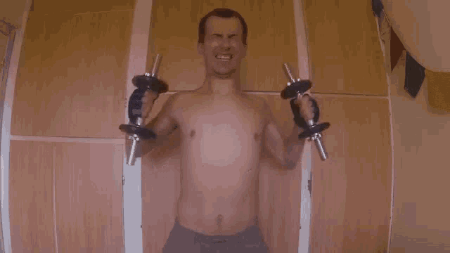 a shirtless man is lifting dumbbells in front of a wall .