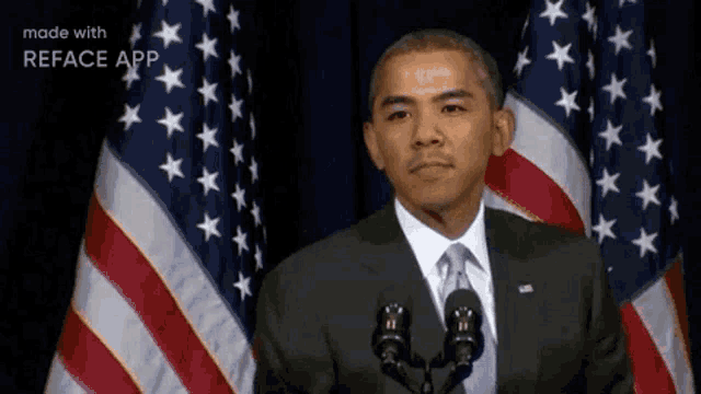 a man in a suit and tie is standing in front of two microphones in front of american flags .