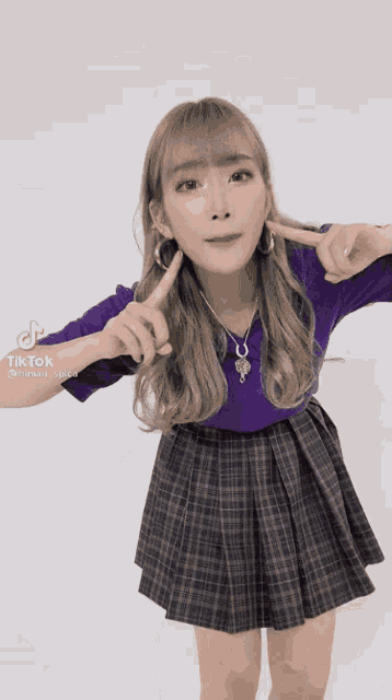 a girl wearing a plaid skirt and a purple shirt is making a funny face .