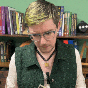 a man wearing glasses and a green vest is looking down at something