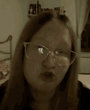 a woman wearing glasses is making a funny face in a bedroom .