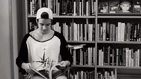 a young man is reading a book in front of a bookshelf with a book titled metallica on it