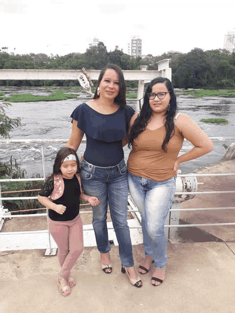 three women standing next to each other on a bridge over a river