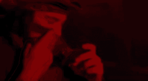 a man with a beard is smoking a cigarette in a dark room in a red light .