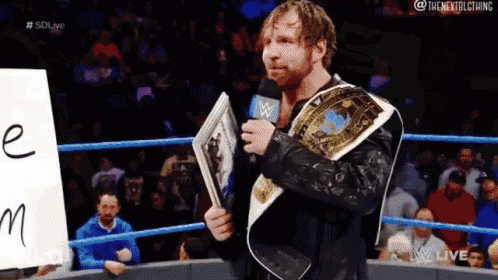 a man in a wrestling ring is holding a microphone and a sign that says e on it