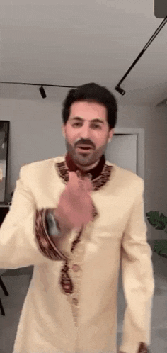 a man with a beard is wearing a tan suit and dancing in a room .