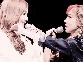 two women are singing into microphones in front of each other on a stage .