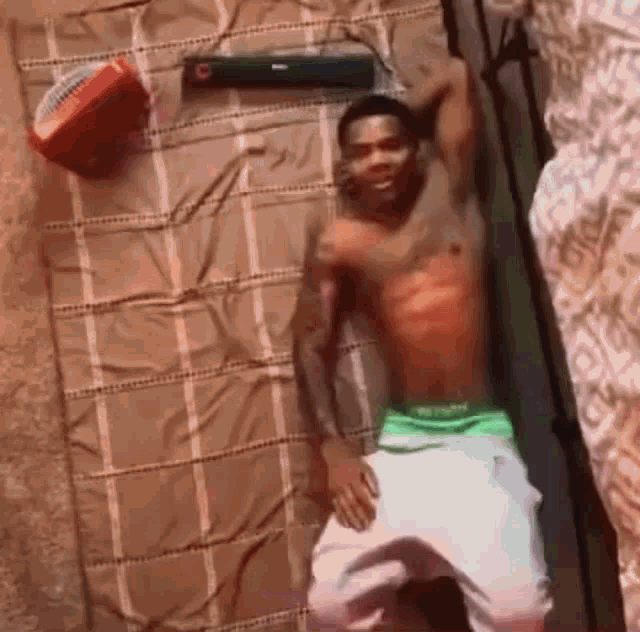 a man without a shirt is laying on a bed with a basketball and a speaker .