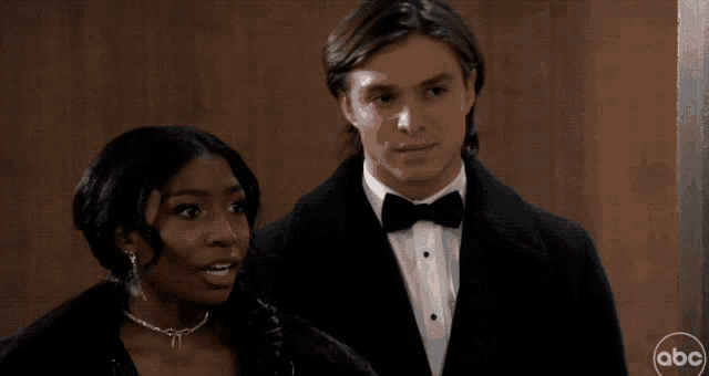 a man in a tuxedo stands next to a woman with abc written on the bottom right corner