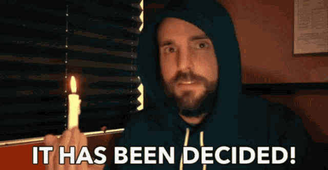 a man in a hoodie holding a lit candle with the words it has been decided behind him