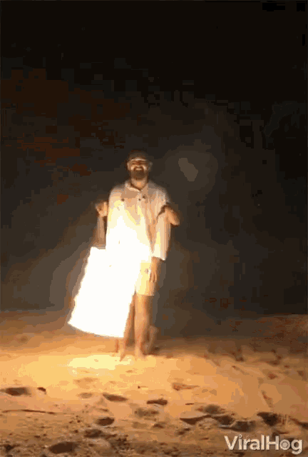 a man standing on a beach holding a bucket of fire with the words viralhog on the bottom right