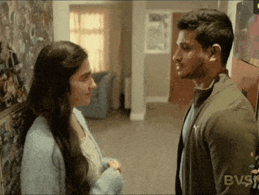 a man and a woman are looking at each other in front of a wall with bvs written on it