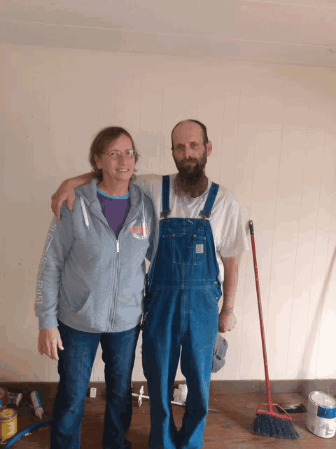 a man wearing overalls stands next to a woman wearing a grey sweatshirt that says ' i love you '
