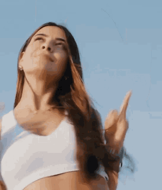 a woman in a white crop top is dancing on a beach .