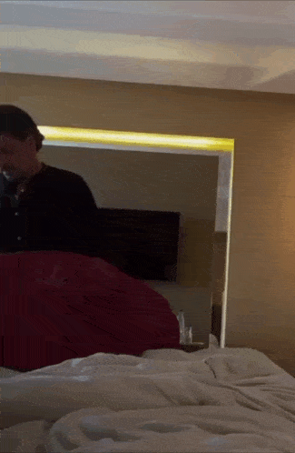 a man in a black shirt stands behind a bed