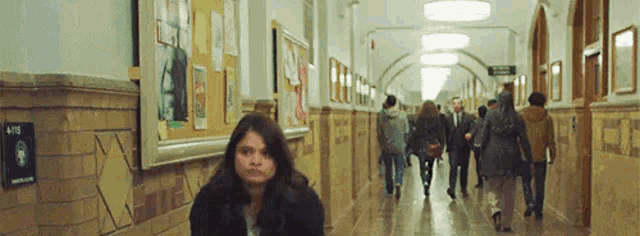a woman is sitting in a hallway in a school while people walk by .