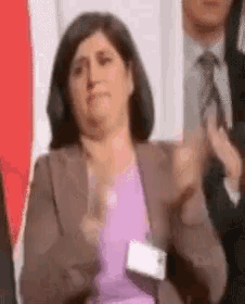 a woman in a suit and tie is clapping her hands .