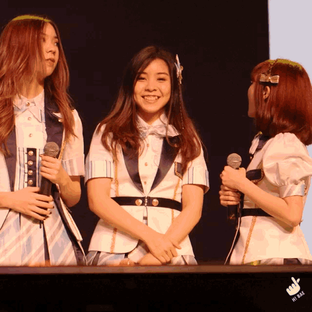 three girls are standing next to each other holding microphones and one of them is wearing a headband with a flower on it