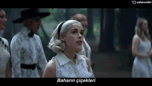a woman in a white dress stands in front of a screen that says " baharin çiçekleri "