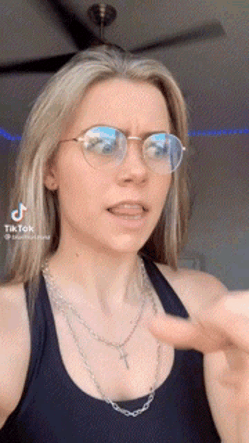 a woman wearing glasses and a necklace is giving a thumbs up .