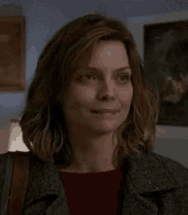 a close up of a woman 's face in a living room . she is wearing a green jacket and a red shirt .