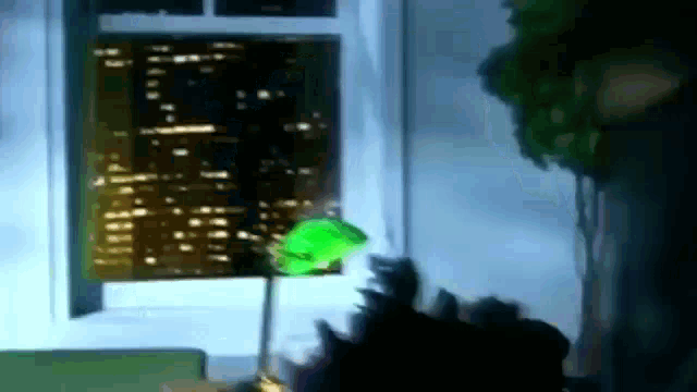 a green lamp is sitting in front of a window with a city skyline in the background .