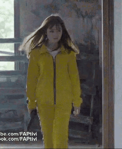 a woman in a yellow jacket and pants is walking through a doorway .