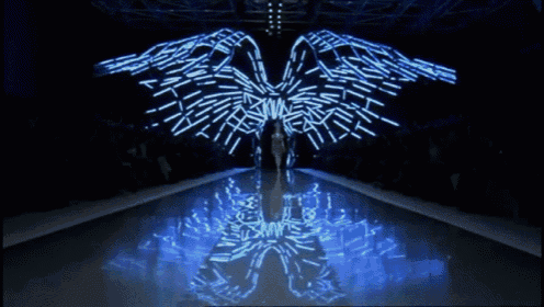 a model walks down a runway at a fashion show with a butterfly design projected behind her