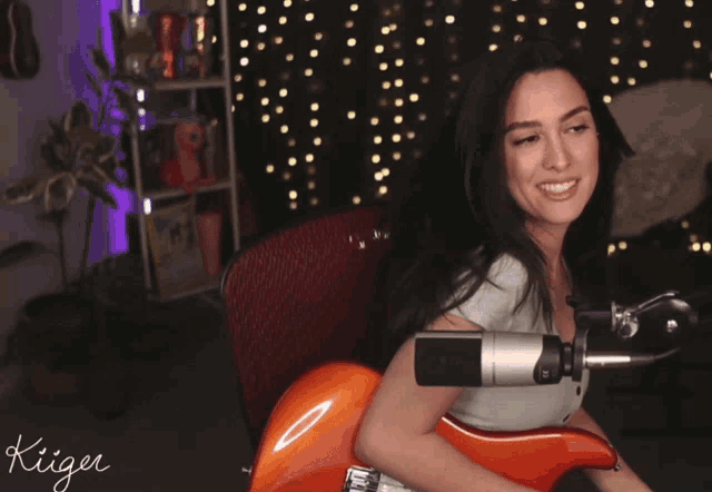 a woman playing a guitar in front of a microphone with the name kiiger written on the bottom