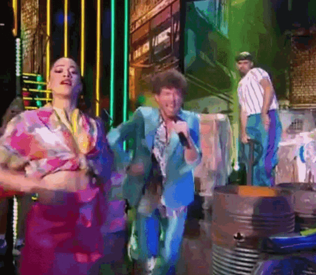 a man in a blue suit is singing into a microphone while a woman in a floral shirt is dancing