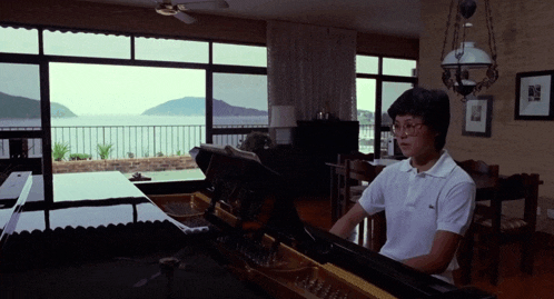 a man in a white polo shirt is playing a piano in a living room