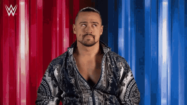 a man with a beard is standing in front of a red and blue background with a w logo