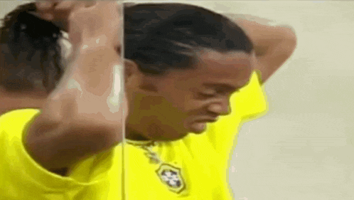 a man in a yellow shirt is looking at his hair in a mirror .