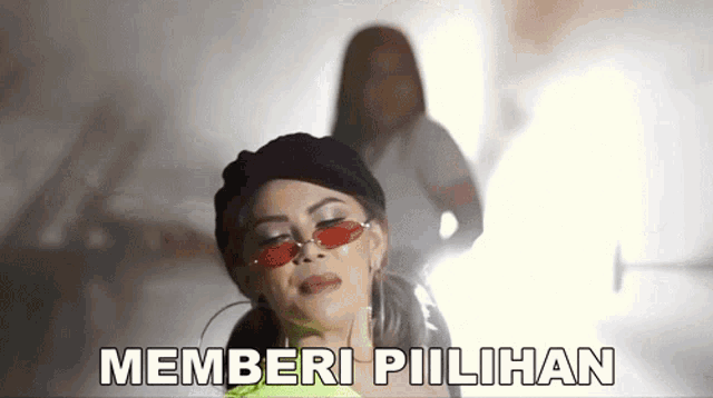 a woman wearing sunglasses and a hat is standing in front of a sign that says " memberi pilihan "