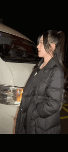 a woman in a black coat is standing in front of a white van at night