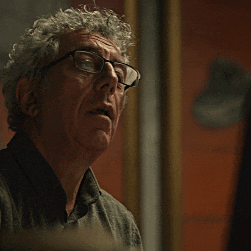 a man with curly hair wearing glasses looks at the camera