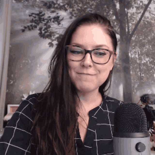a woman wearing glasses and a plaid shirt stands in front of a microphone