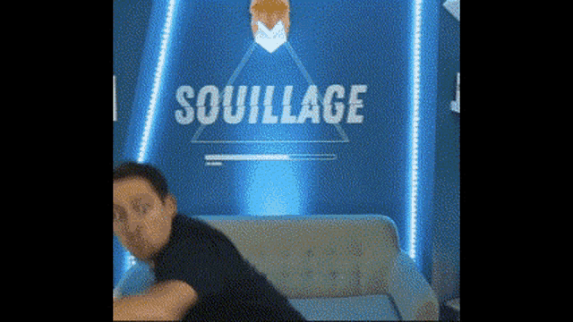 a man is sitting on a couch in front of a sign that says souffle .
