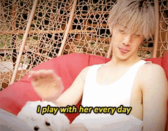 a man in a white tank top sits in a chair with a dog and says i play with her every day