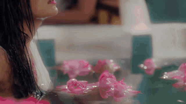 a woman in a bathtub with pink flowers floating in it