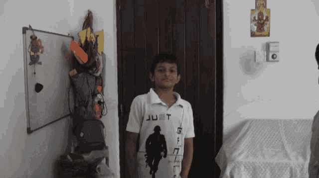 a boy wearing a shirt that says just standing in front of a door