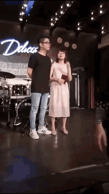 a man and a woman are standing on a stage in front of a sign that says delicus