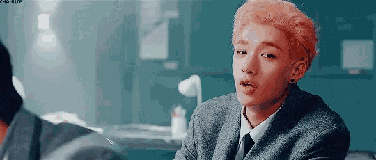 a young man with pink hair is wearing a suit and tie and sitting in a room .